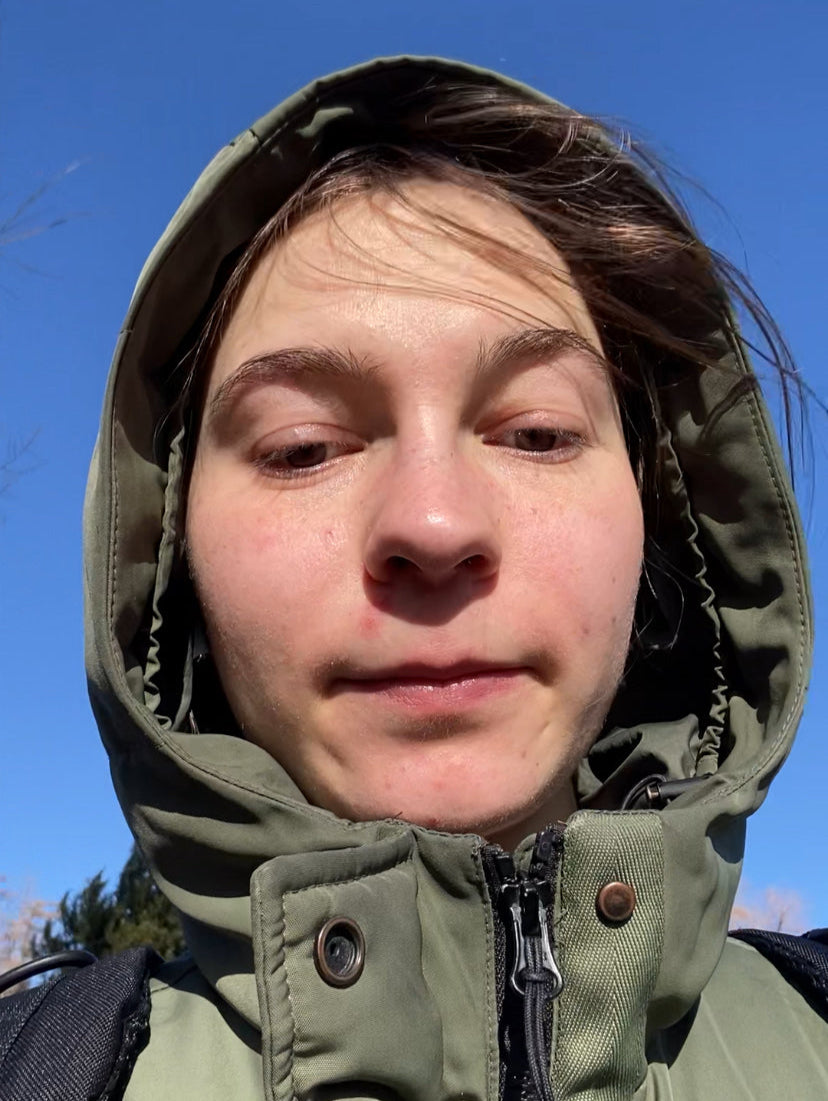 Person wearing a green hooded jacket against a blue sky